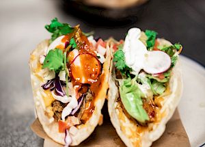 Two tacos filled with various ingredients including meat, avocado, radish, cilantro, and sauce, served on a plate topped with a napkin.