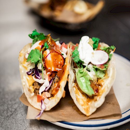 Two tacos filled with various ingredients including meat, avocado, radish, cilantro, and sauce, served on a plate topped with a napkin.