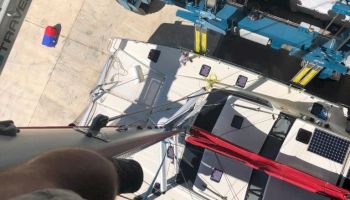 A person is looking down from a height with a view of industrial machinery below, including a large blue crane and work equipment on the ground.