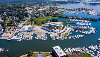 This image shows an aerial view of a coastal town with numerous boats docked in a marina, surrounded by buildings and greenery.