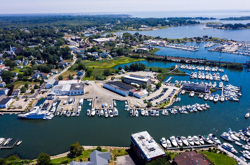 This image shows an aerial view of a coastal town with numerous boats docked in a marina, surrounded by buildings and greenery.