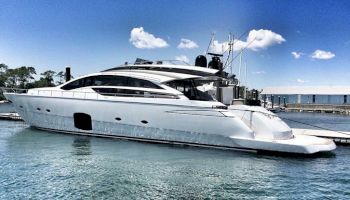 A sleek white yacht docked at a marina on a sunny day with a clear blue sky and a few clouds.