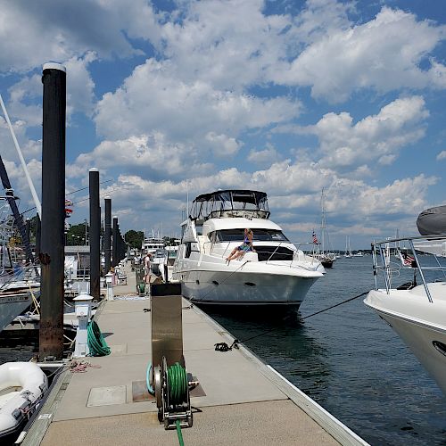 A dock with several boats tied up, one large white boat prominently in the center, under a partly cloudy sky.