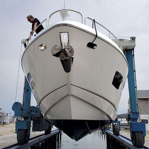 A large white boat is being lifted by a blue boat lift, with a person standing on the deck.