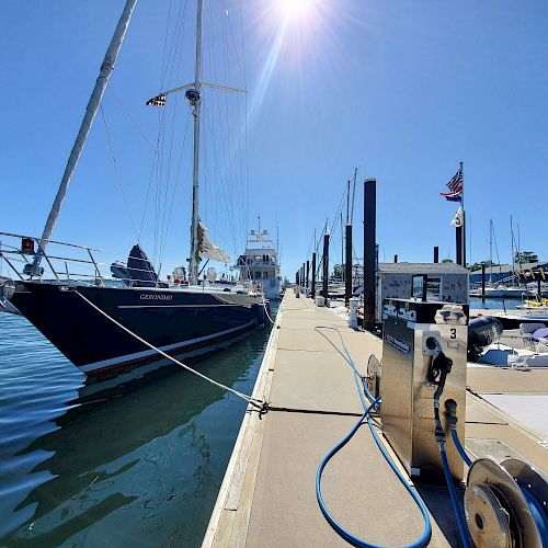 A docked sailboat in a marina with a sunny sky in the background and various other boats tied along the pier.