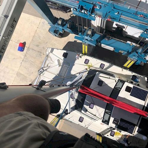 The image shows a view looking down from a height, focusing on industrial equipment, possibly on a crane, and a person’s knee in the bottom left corner.