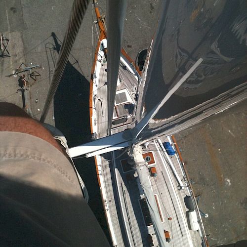 A view looking down from the mast of a sailboat, with sails visible and part of a leg in the frame, highlighting the height and perspective.