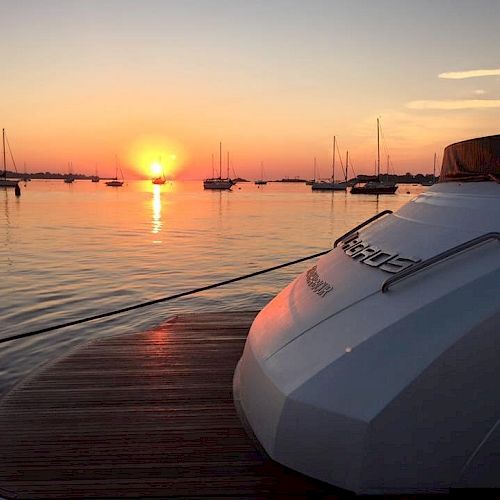 A serene sunset over a harbor filled with anchored boats, captured from the deck of a luxurious yacht.