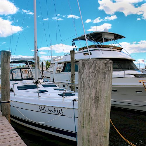 Several boats docked at a marina on a sunny day, with blue skies and clouds in the background.