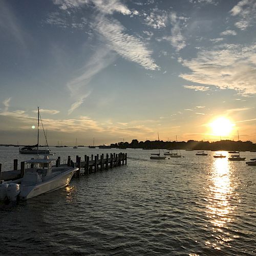 A serene sunset over a harbor with several boats docked and gentle waves reflecting the golden sky, completing a peaceful scene.