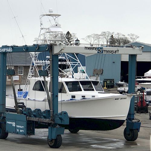 A white boat suspended by a large blue Marine Travelift with 