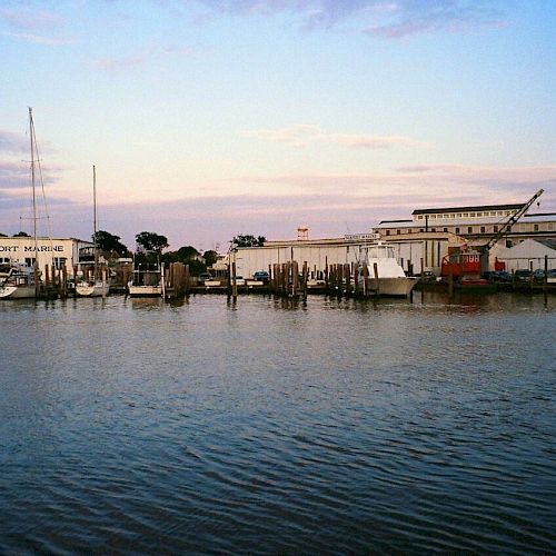 The image shows a calm waterfront scene with boats docked by buildings and structures at sunset, featuring a peaceful harbor ambiance.