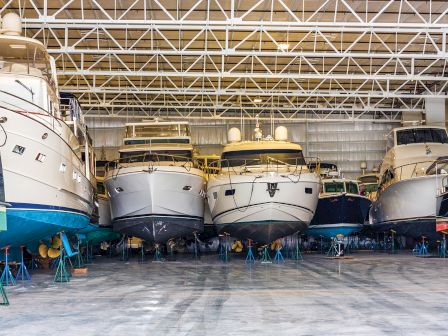 This image shows several boats stored in a large indoor facility with a metal roof structure, all propped up on stands.