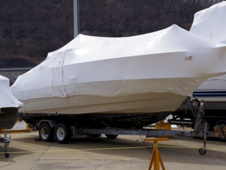 The image shows a boat covered in a protective tarp, situated on a trailer, parked in an outdoor area.