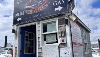 The image shows a small marina shack with signs indicating diesel and gas availability, featuring a welcome sign and a U.S. flag.