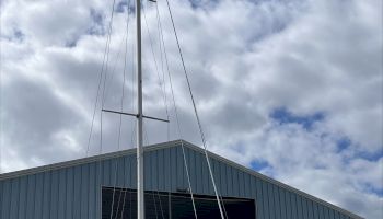 A sailboat is on dry ground in front of a large blue warehouse, under a partly cloudy sky.